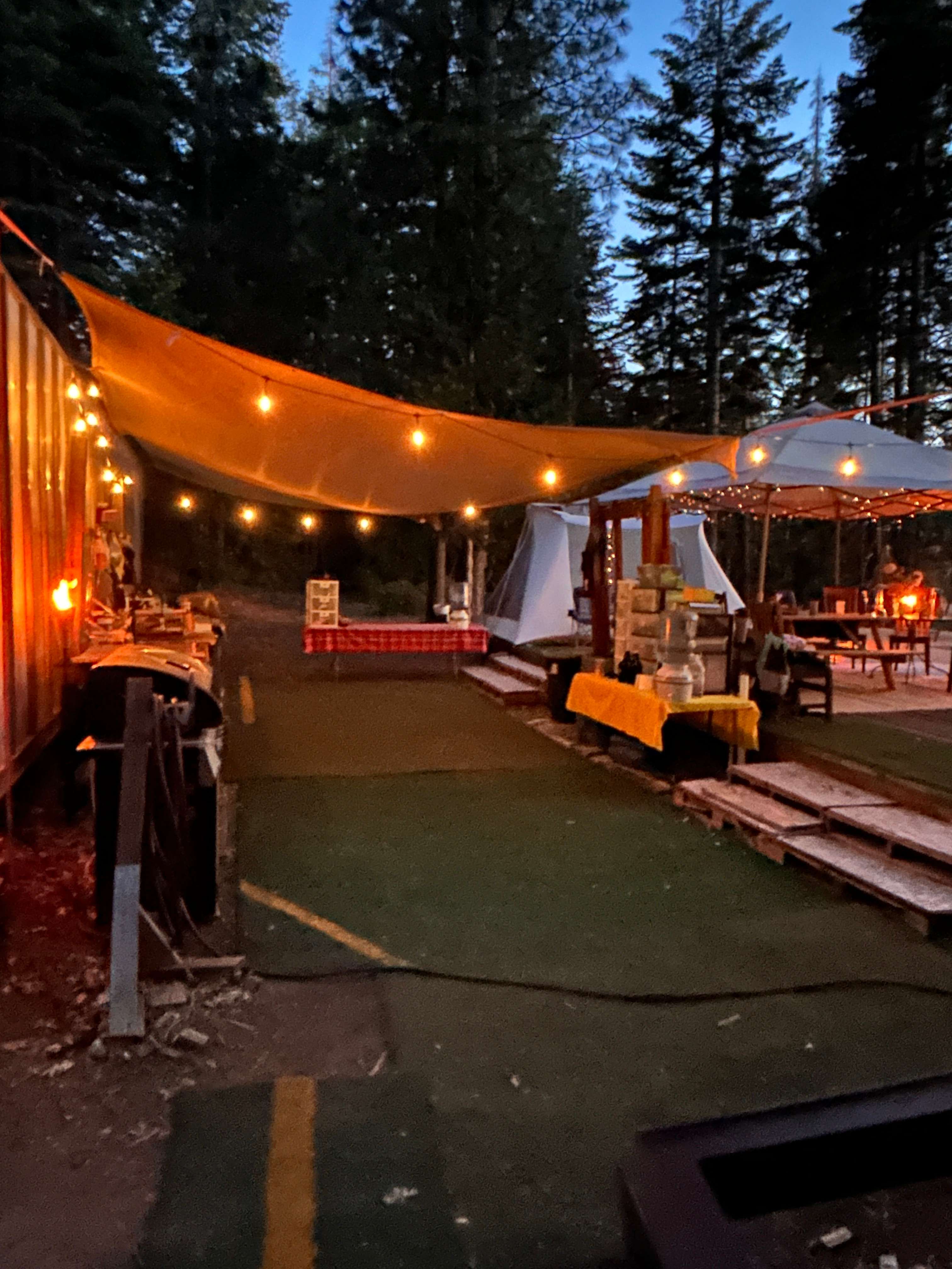 10x14 Kodiak Canvas Tent on the large deck, adjacent to the communal kitchen, dining area with multiple picnic tables, and the Domed fire pit. 