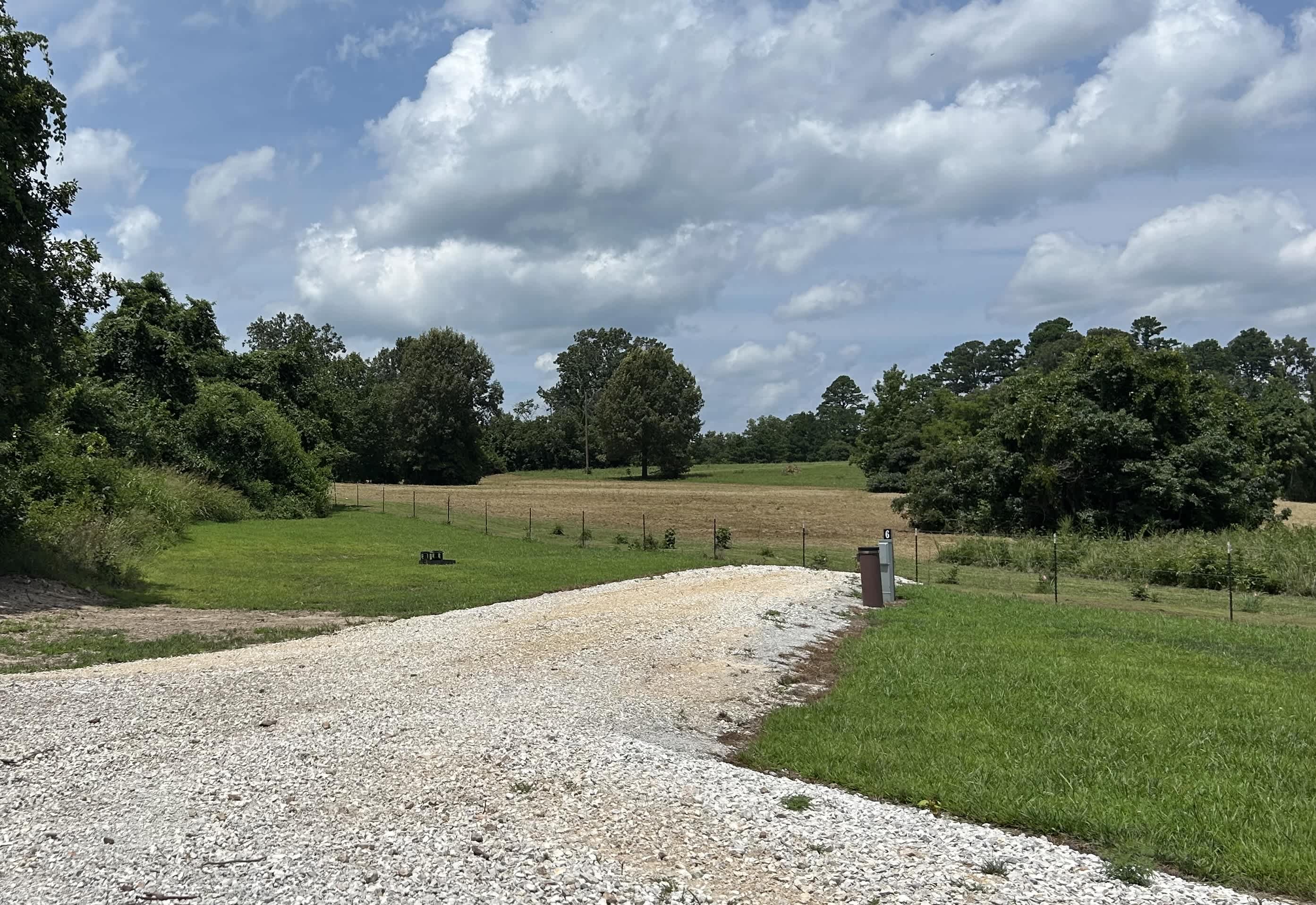 View of Site 6, which is a back-in, approximately 72' in length. LOTS of room to spread out! This site is shaded in the evenings.  If there isn't enough room for your vehicle(s) to park within the site itself, you may park at the edge of the roadway adjacent to your site. Please, only two wheels in the grass and be mindful of the space other park visitors will need when driving/towing their RV past your vehicle. Please do not drive across the erosion control devices we have in place.