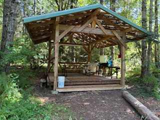 Communal outside kitchen area complete with drinking water, gravity feed water for two pan sink, 3 burner propane stove, picnic table and food prep table.