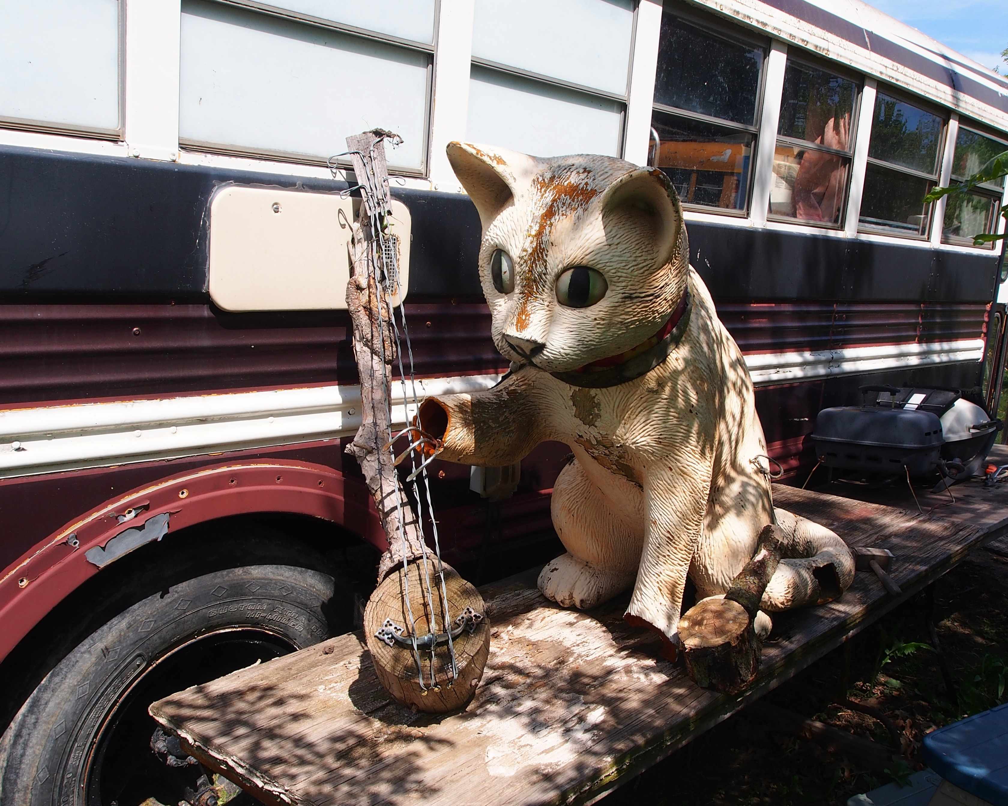 Cat Statue with an original work of art depicting a stringed instrument using barbed wire and other scrap materials.