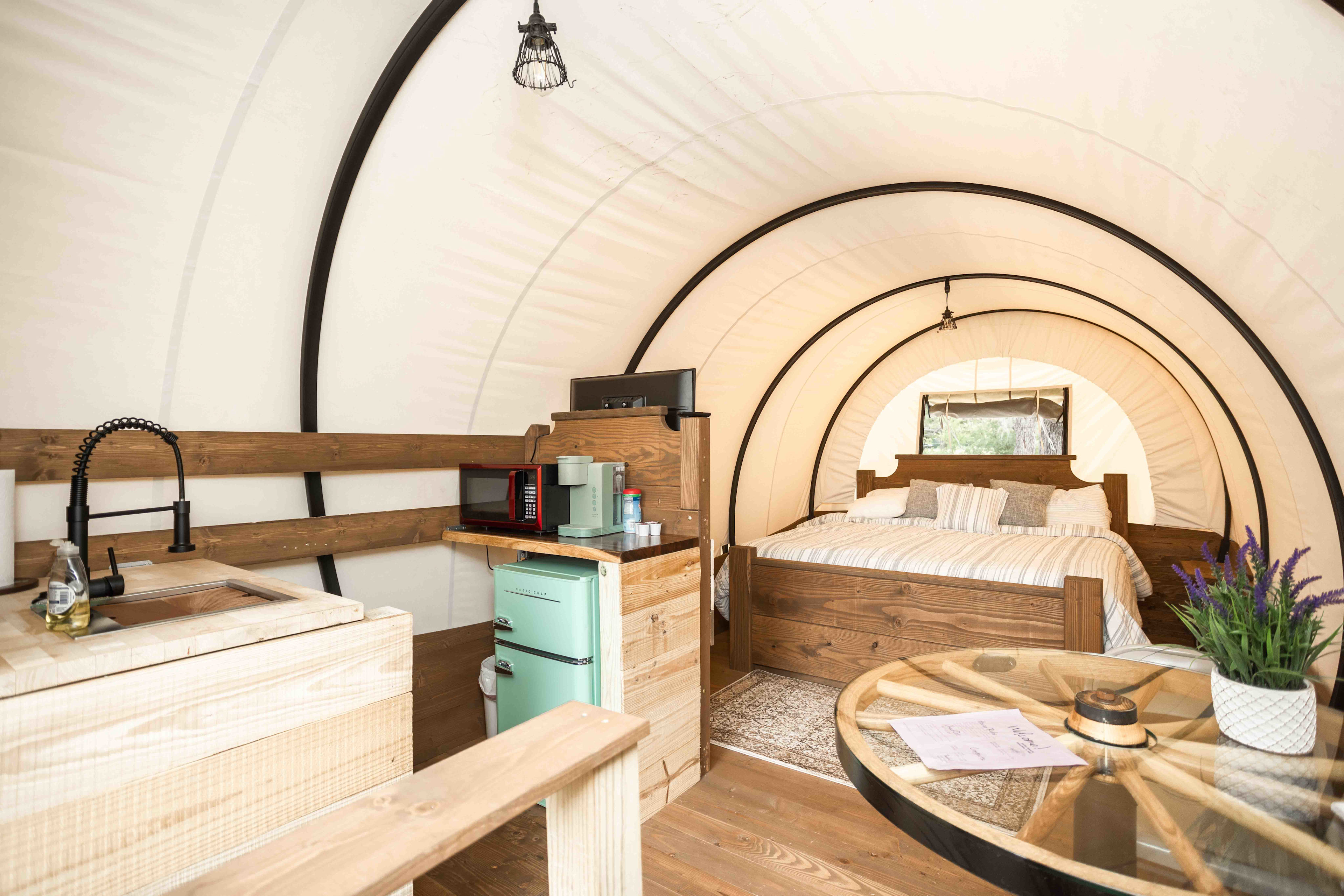 Conestoga wagon interior with king size bed, kitchenette, dining table, and tv. 