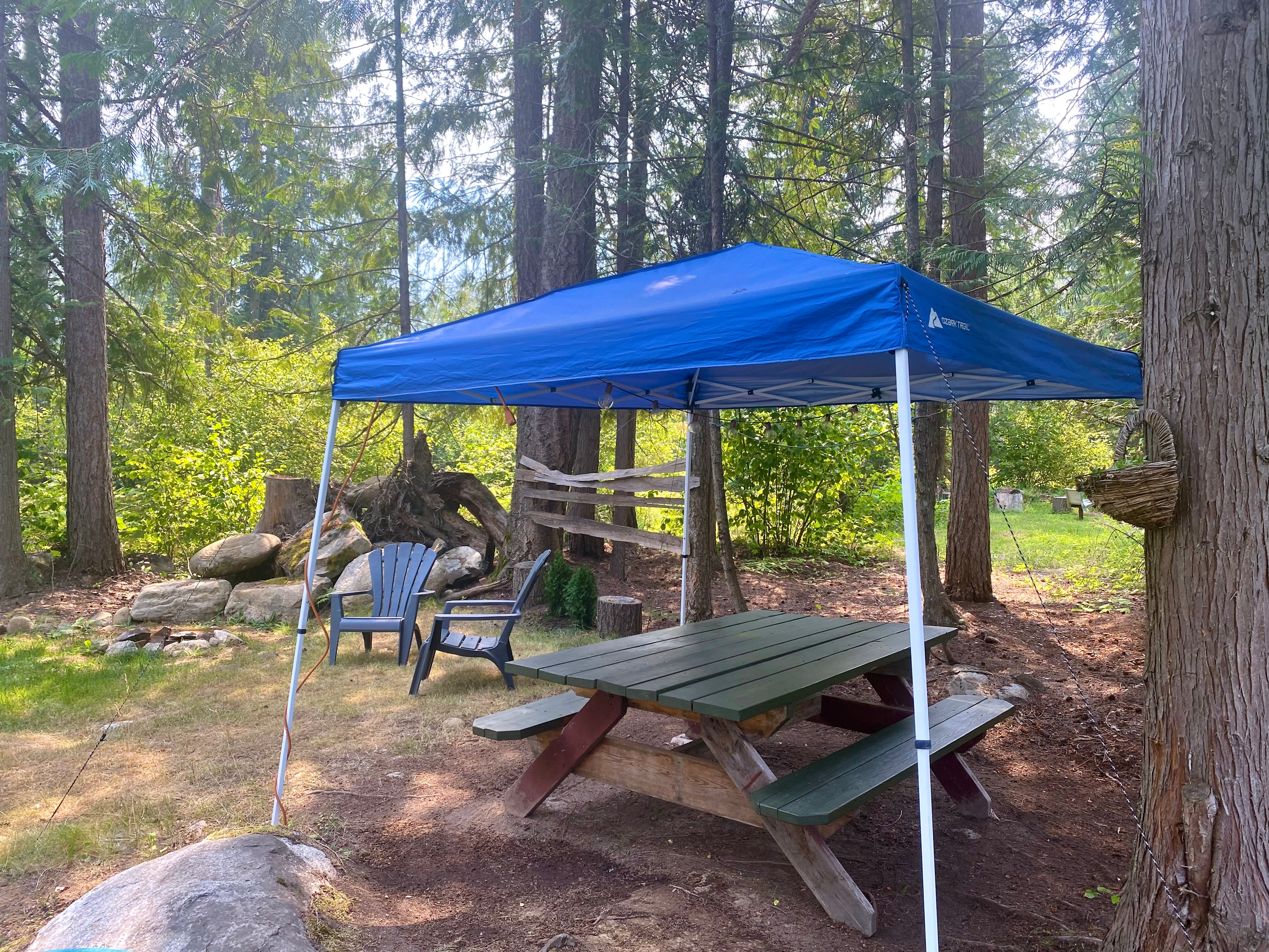 Outdoor picnic table with covered canopy. Two chairs provided to relax in around the fire pit. The trees surrounding the glamping area provide shade and privacy from the main house. 