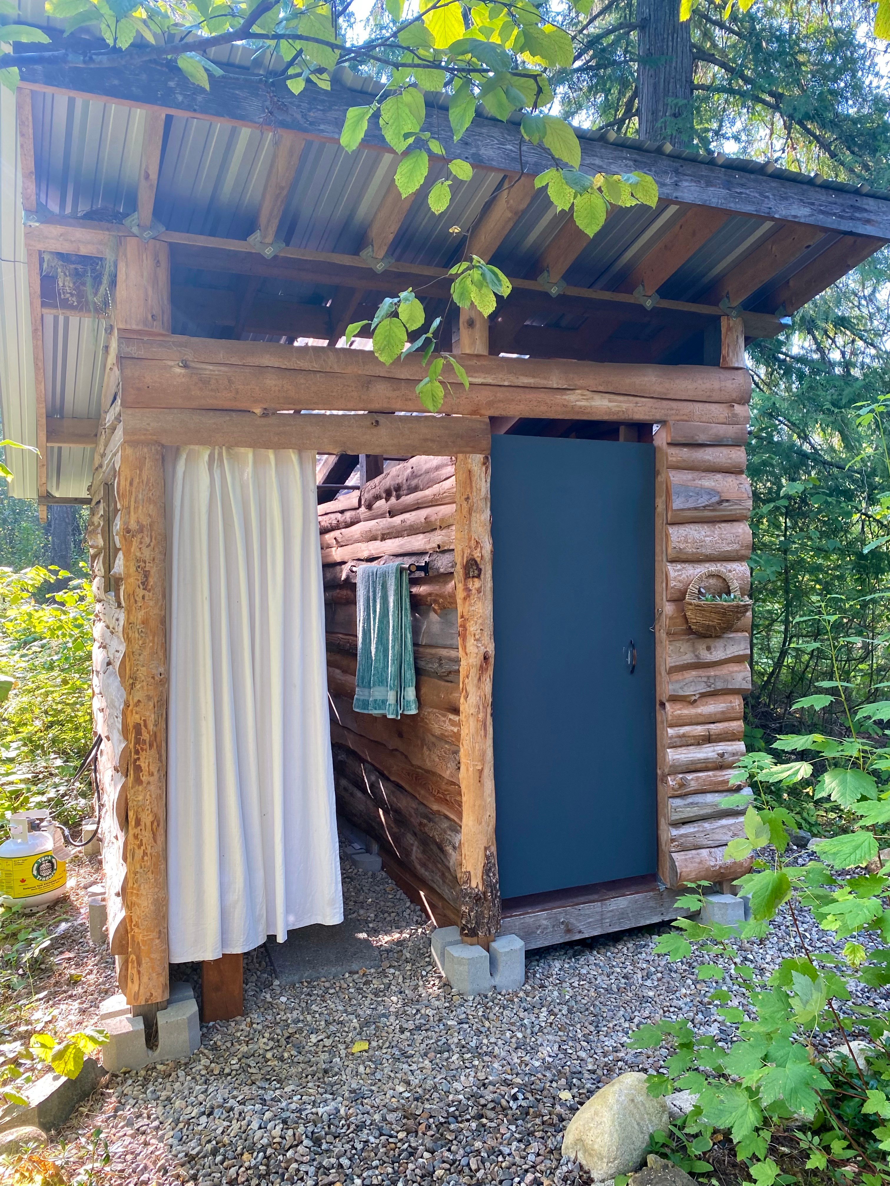 Outdoor bathhouse with off grid hot water shower on one side with composting toilet and basin sink on the other side.