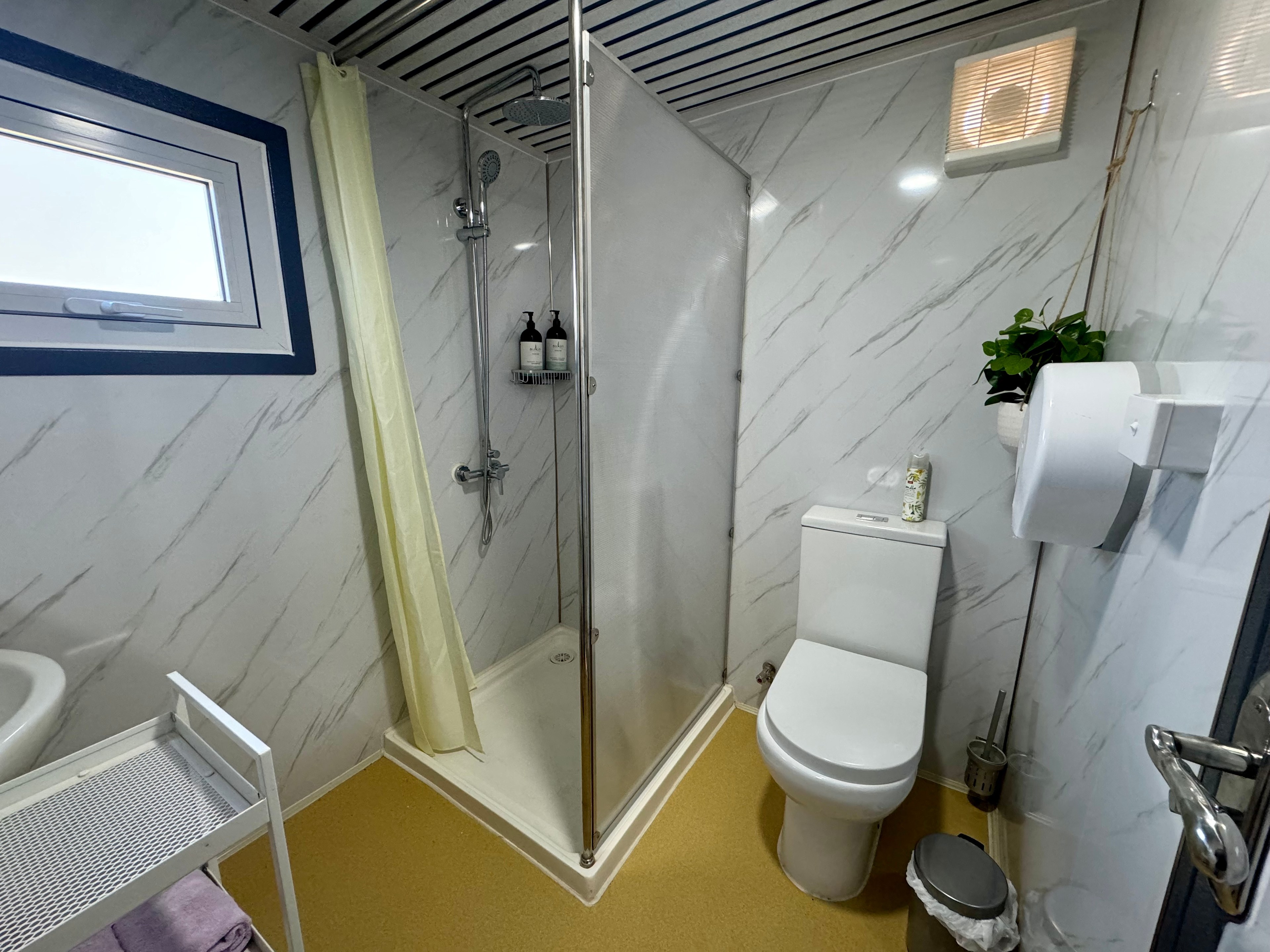 Bathroom facility interior - flushing toilet, shower and vanity basin - basic toiletries and towels provided. 