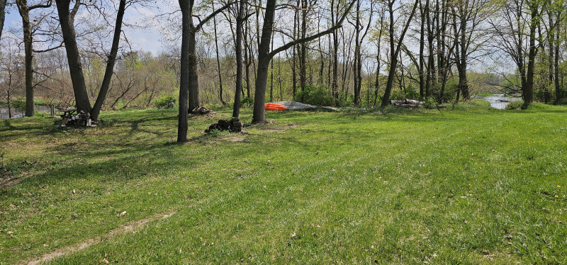 Riverside campsite with fire pit, picnic table, and hammock stand.