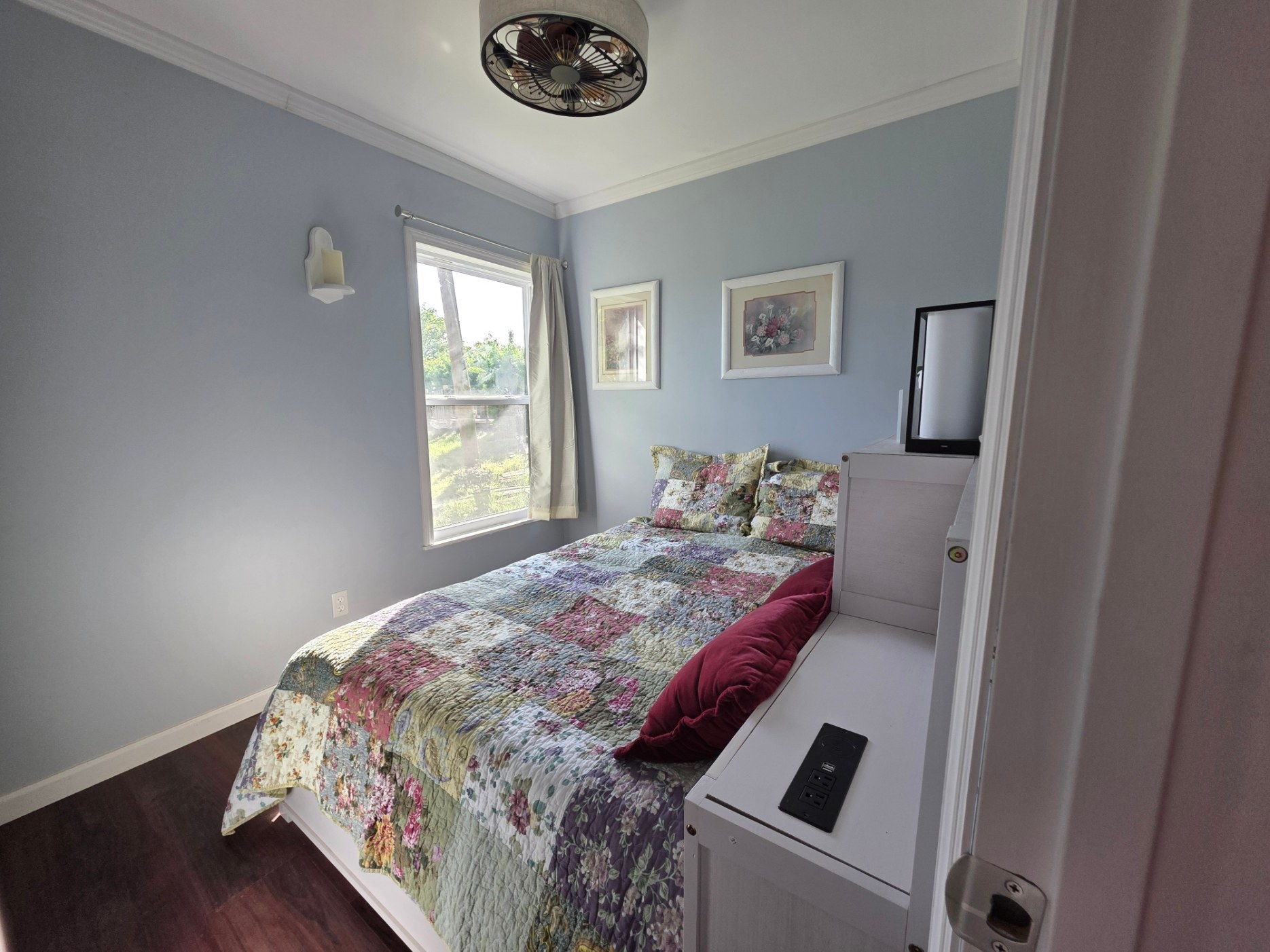 The bedroom is small. Its full-size captains bed has three drawers and a bookcase.  It also has a charging station and small lamps.  The window overlooks the land that slopes down into the woods toward the lake.  The wall sconce next to the window bears an LED candle.