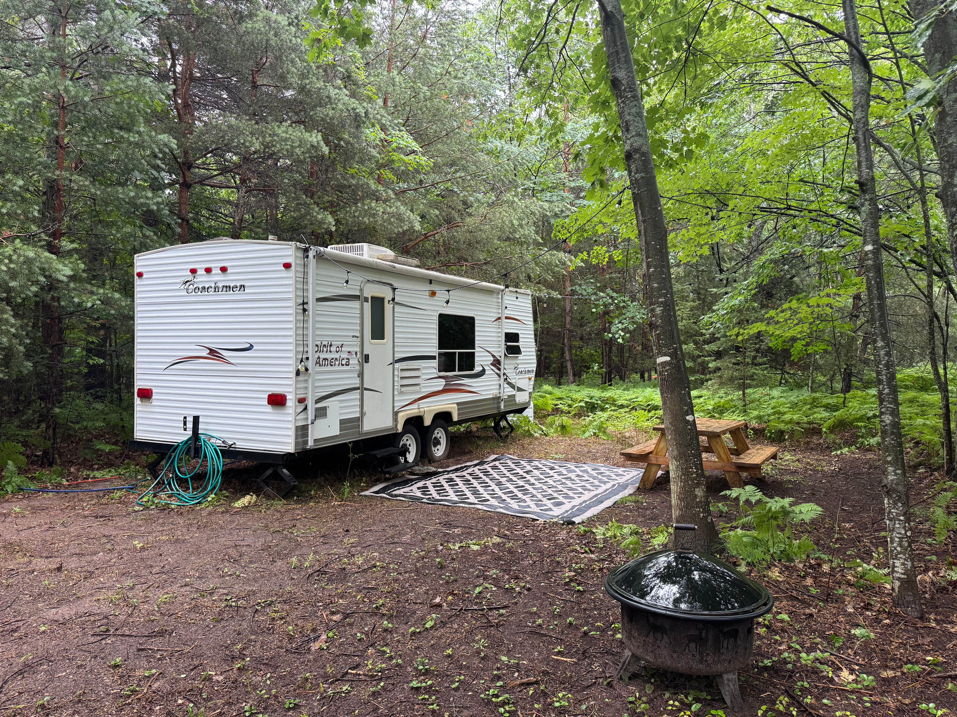 Camper and site with picnic table outdoor carpet lights, outdoor hose and fire pit.