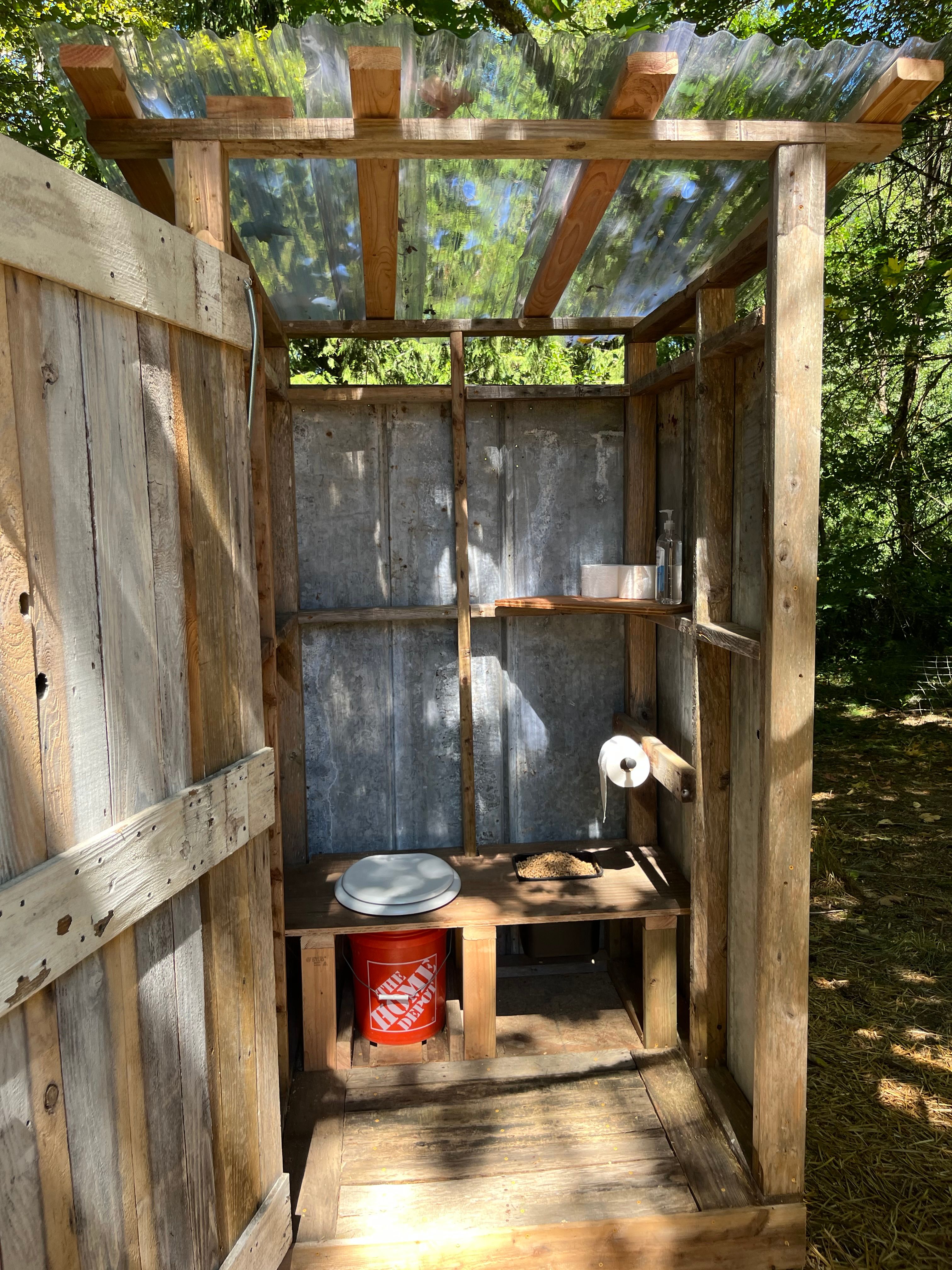 Outhouse features: clear plastic roof for light, inside locking door, composting toilet, wood pellets for smell, toilet paper, and hand sanitizer.