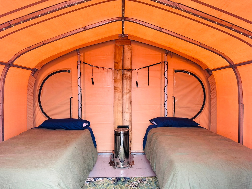 Weatherport Tents include (2) single beds *can be rearranged into one bed with cozy bedding, Nordic stove, bench and hanging lights.