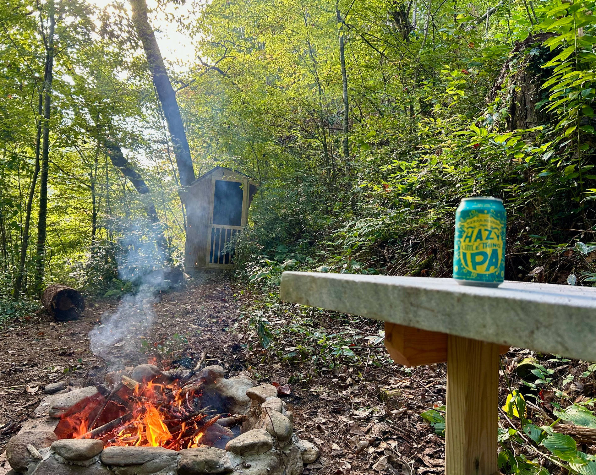 A table for 2 in front of the firepit. The outhouse can be seen in the background.