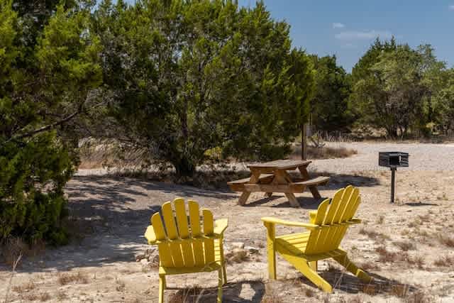 Mulched Campsite nestled in the trees with Adirondack chairs, picnic table, fire pit and grill.
