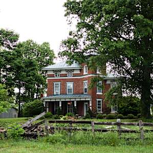 The main house on the property. Beautiful building surrounded by gorgeous trees and landscaping. The plants are well manicured and the grass is trimmed.