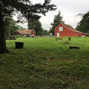 view of the barn and port a potty from site 4- communal large fire circle visible off to the left in middle of field. One common picnic table near fire circle.