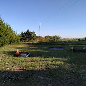 Each site features a picnic table, firepit with cooking grate, and fixed tarp for your tent. This is a picture of site #2.