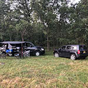RVs set up outside the fence at the north edge of the wooded area. There is shade from the woods, as well as a few spaced out large trees.