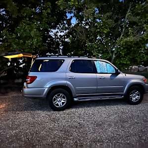 Behind the car is a spot to put chairs or a table on the gravel and the car is facing a house.