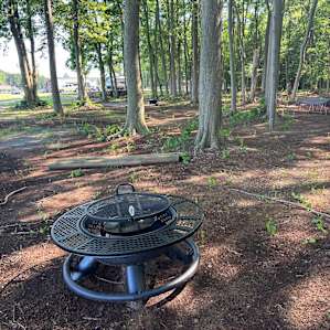 Tent site fire pit/ grill with bath house behind and bench seating coming soon