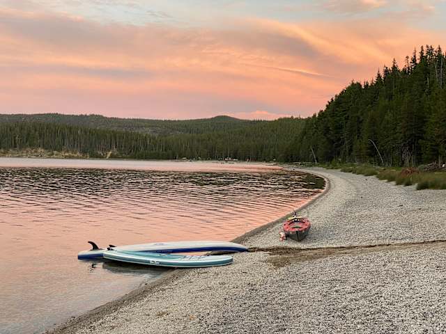 Sunset over a lake with a paddleboard and boat resting on a gravel beach