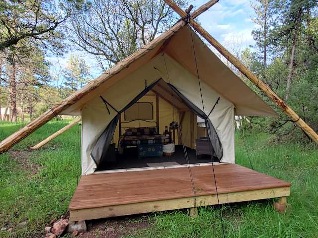 Canvas glamping tent with wooden deck set in a green meadow with trees