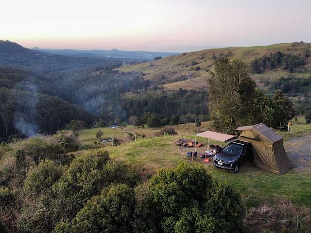 Aerial view of a tent and truck campsite on a ridge at dusk overlooking forested valley