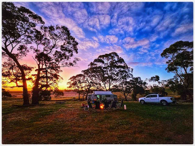 Caravan and truck camp at sunset under mackerel sky with silhouetted trees