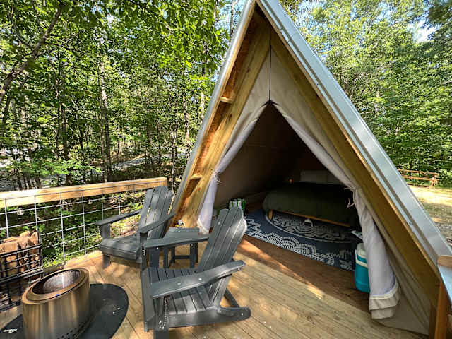 Canvas A-frame glamping tent on a wooden deck surrounded by forest