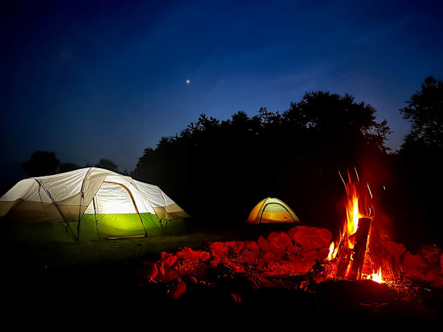 Two illuminated tents beside a campfire under a starry twilight sky at treeline