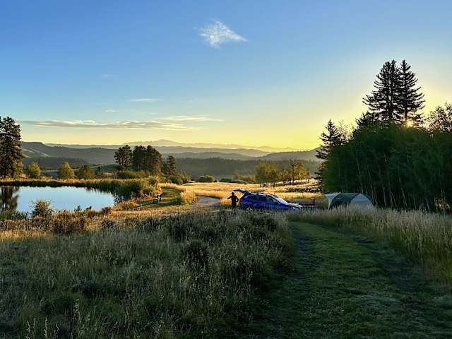 Tent and car beside pond at sunrise, mountains and aspens in golden light