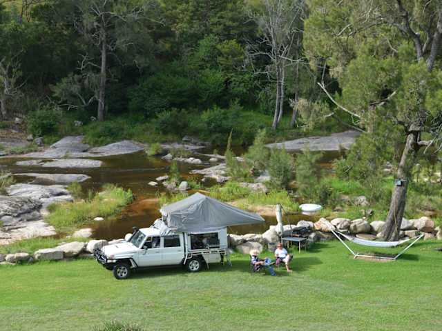 Off-road truck with rooftop tent parked by rocky river, campers relaxing nearby