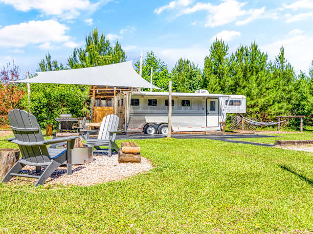 Adirondack chairs and fire pit facing a converted horse trailer glamping unit under a shade sail