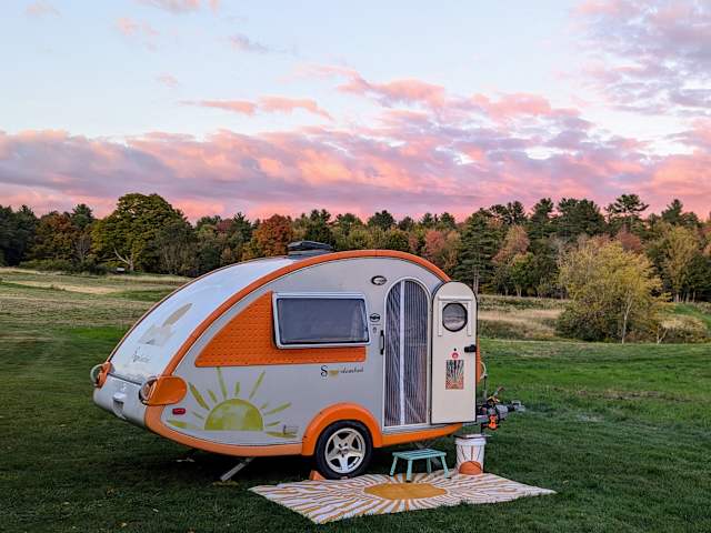 Orange and white teardrop camper trailer on grass at sunset with pink clouds