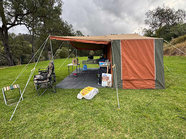 Tent camp on grassy bank overlooking a bend in a forested river valley