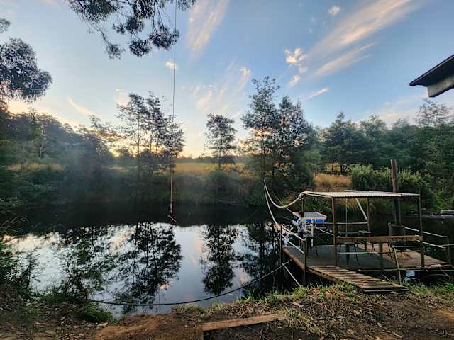 River at dusk with rope swing, dock, and misty tree-lined banks reflecting sunset sky