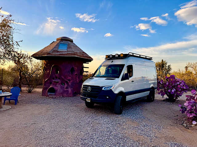 Overland van parked beside a rounded stone cabin at golden hour in the desert