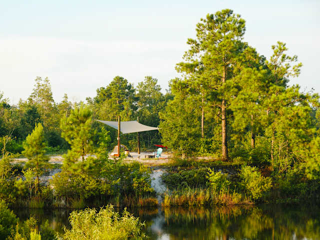 Shade sail and campsite nestled among tall pines beside a calm lake at golden hour