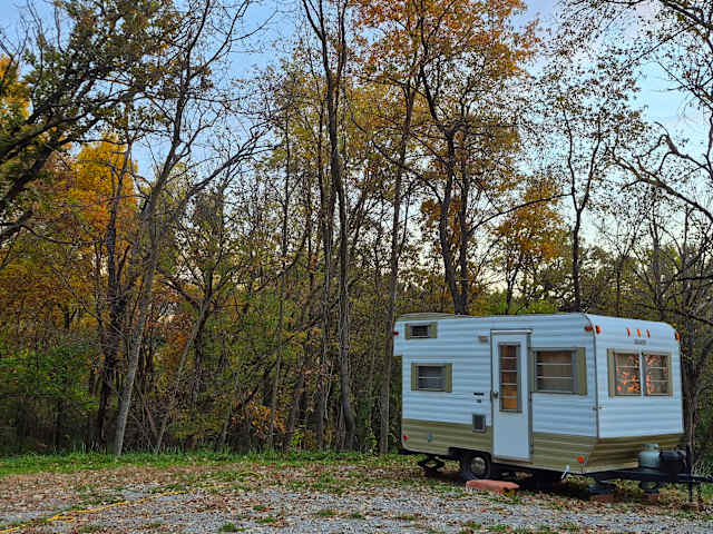 Vintage white camper trailer parked before autumn-colored forest at dusk