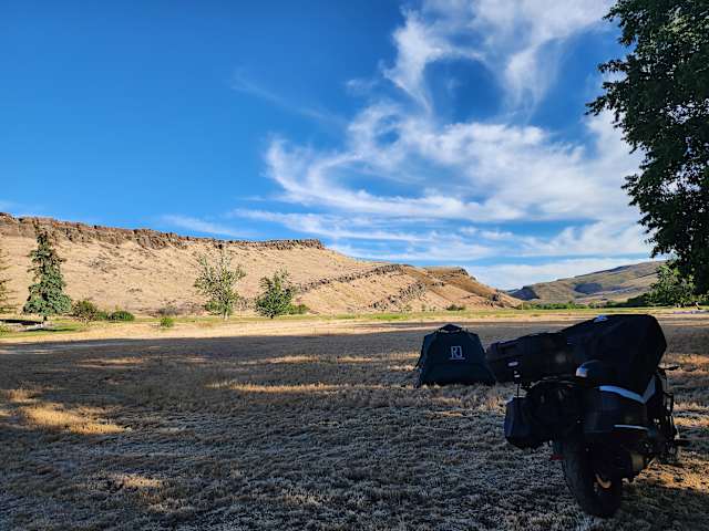 Rooftop tent and motorcycle camp at dusk beneath golden sandstone bluffs and wispy clouds