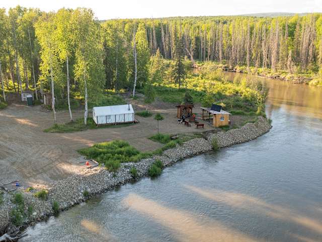 Aerial view of riverside camp with white tent, cabin, and picnic area at sunset