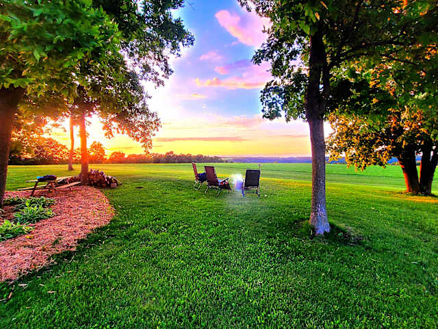 Camp chairs and fire pit glowing under pink and gold sunset over open field
