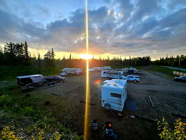Sunset over treeline with sun flare, RVs and trailers parked in campground clearing
