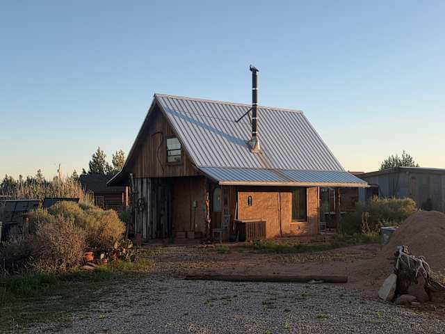 Wooden cabin at dusk with fire pit glowing, moon overhead, dog standing nearby