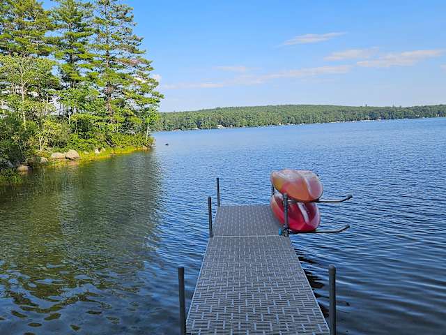 Aluminum dock extending into calm blue lake with a red kayak resting on it, pine trees lining the shore