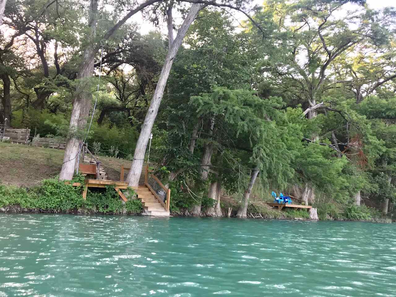 a water view showing both docks. the one on the left has rope swings, and steps for entering and exiting the river with floats, kayaks, SUPS, etc. The one on the right, is better suited for fishing, relaxing, meditating. There is a steel ladder adjacent to it.