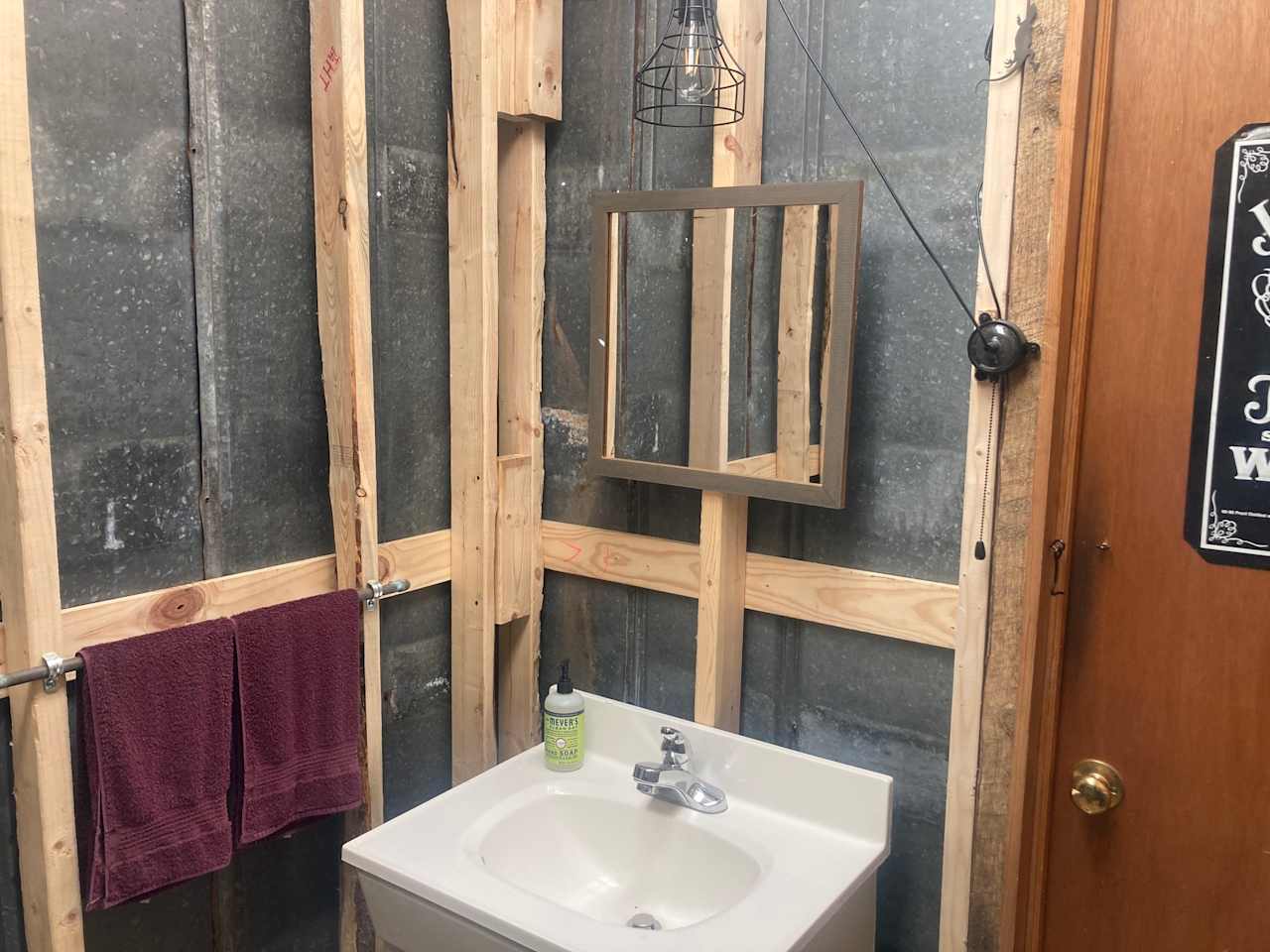 Outhouse interior with foot pump sink, solar light, towels, and hand soap