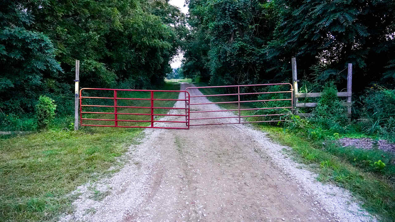 Front gravel driveway entrance with red metal gate. 
