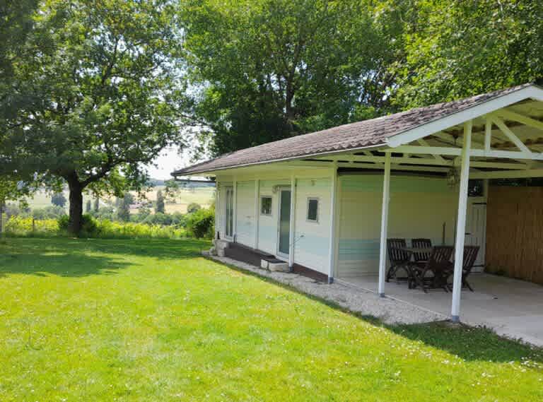 Mobile home with outside seating on covered patio, with grass area to be enjoyed.