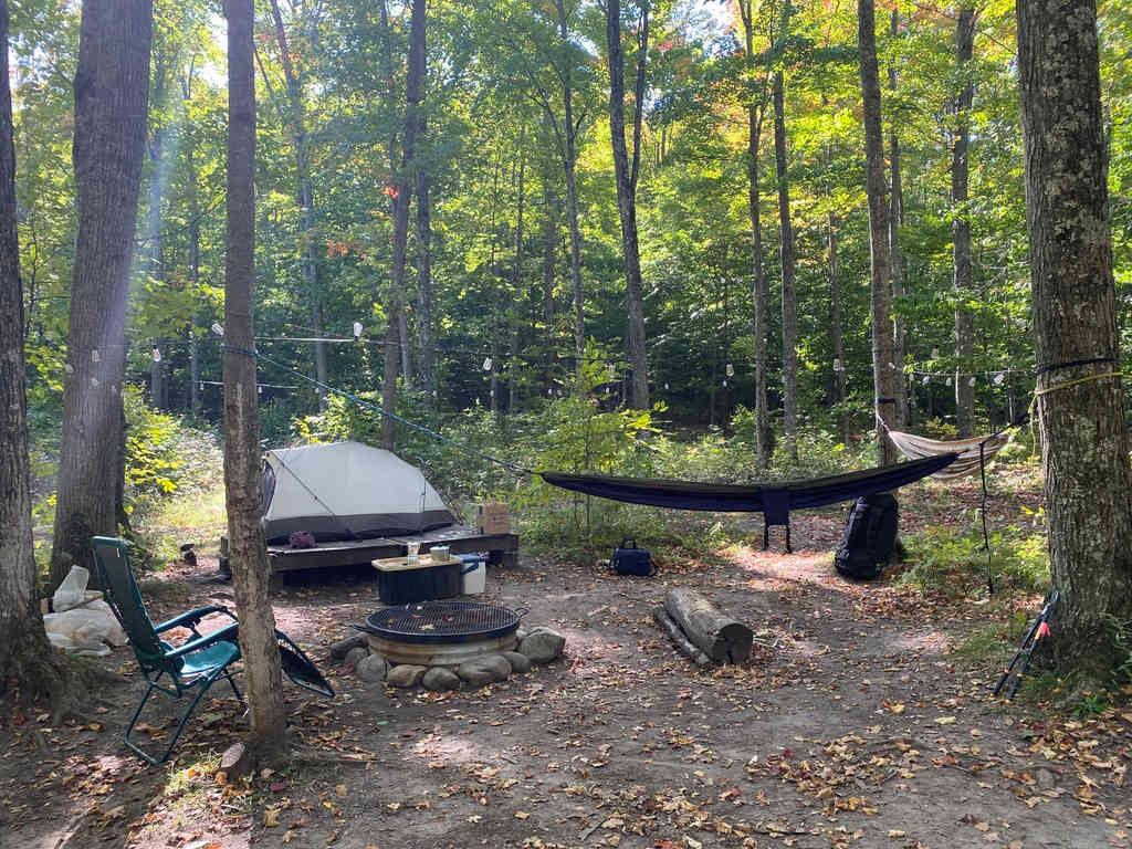 A camp set up around the fire pit in the wooded area next to the parking. 