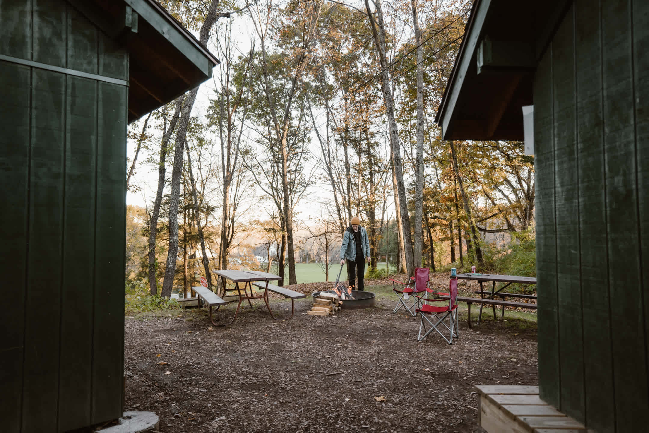 Two shelters side by side with a campfire ring and two picnic tables.