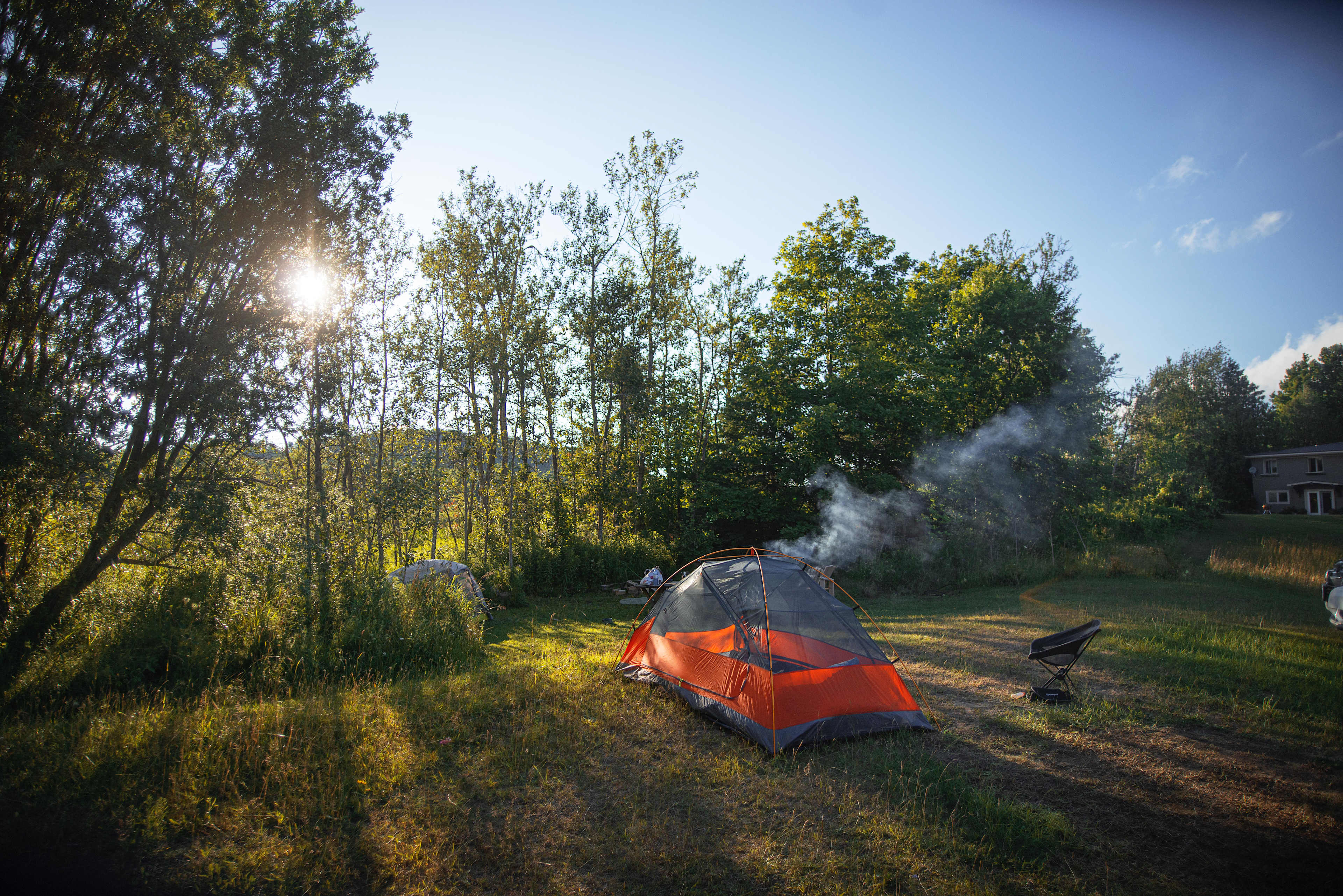 View of site with tents, fire going, and house in the distance.