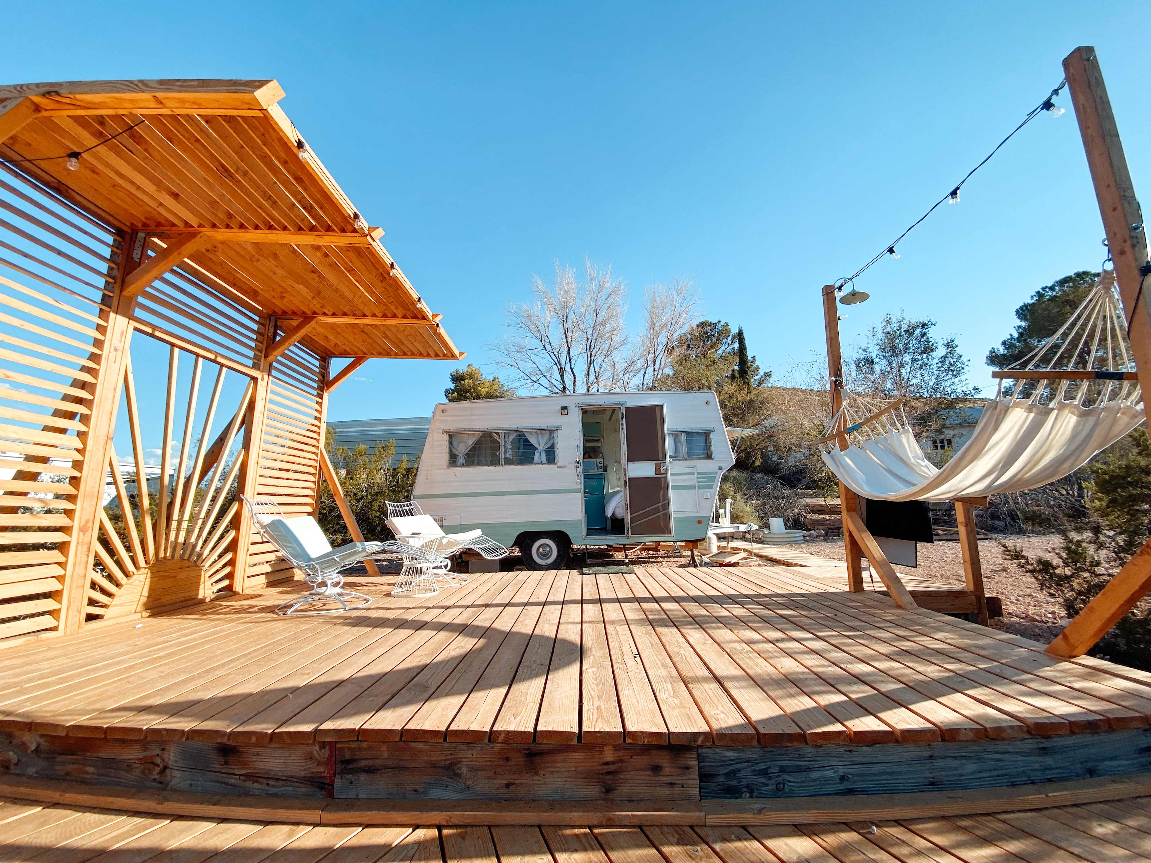 Vintage camper with full deck, hammock, and lounge chairs. 